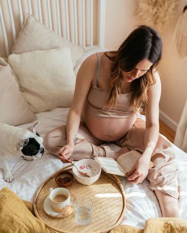 A pregnant woman reading and having breakfast in bed